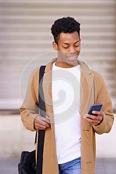 Smiling black man looking at his smartphone while walking down the street.