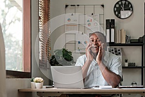 Smiling black man using laptop at home in living room. Happy mature businessman send email and working at home. African
