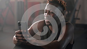 smiling black man is using smartphone in gym, after workout, portrait of african athlet