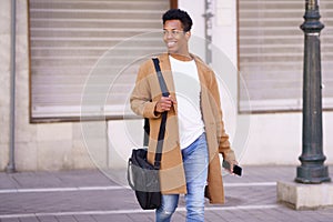 Smiling black man walking down the street carrying a briefcase and a smartphone in his hand.