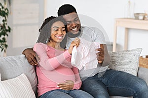 Smiling black pregnant couple holding baby clothes