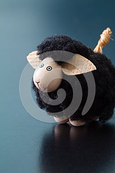 Smiling black sheep toy figurine with big ears on a blue surface