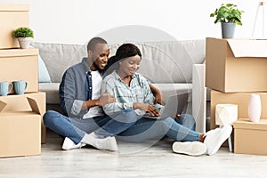 Smiling Black Sposes Sitting With Laptop Among Cardboard Boxes In New House