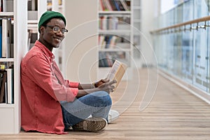 Smiling Black student man reading book in university library , looking at camera. Reading hobby.