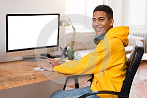 Smiling black teen guy at computer desk with blank screen