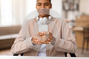 Smiling black teen guy with headphones using smartphone
