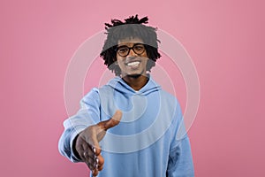 Smiling black teenager offering handshake greeting on pink studio background. Partnership, deal or agreement concept