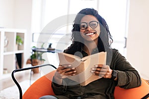 Smiling black woman in glasses reading book and posing