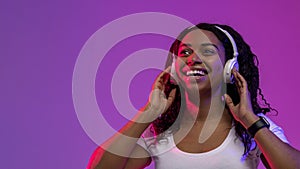 Smiling Black Woman Listening Music In Wireless Headphones Under Neon Lighting