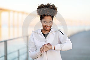 Smiling Black Woman Looking At Smartwatch, Checking Sport Activity After Outdoor Training