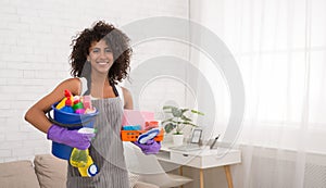 Smiling black woman posing with cleaning supplies