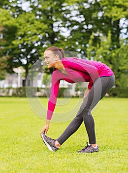 Smiling black woman stretching leg outdoors