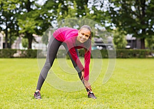 Smiling black woman stretching leg outdoors