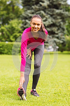 Smiling black woman stretching leg outdoors