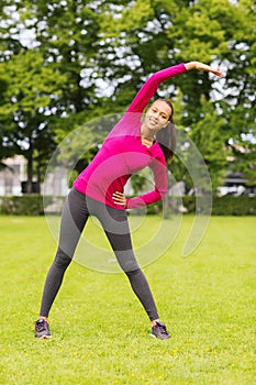 Smiling black woman stretching leg outdoors