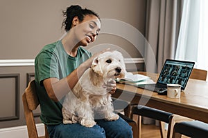 Smiling black woman stroking her dog while sitting at home