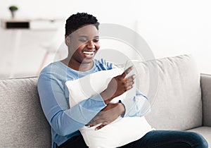 Smiling black woman using mobile phone, holding pillow