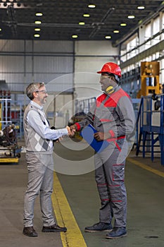 Smiling Black Worker in Protective Workwear And Smiling Caucasian Production Manager Shaking Hands In A Factory