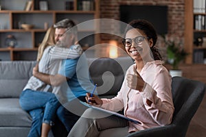 Smiling black young doctor in glasses show thumb up approves therapy of mature european couple