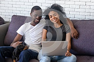 Happy black couple using laptop relaxing with pet at home photo