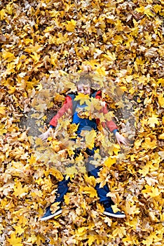 Smiling blond boy lies strewn with yellow autumn leaves. Top view. Autumn concept