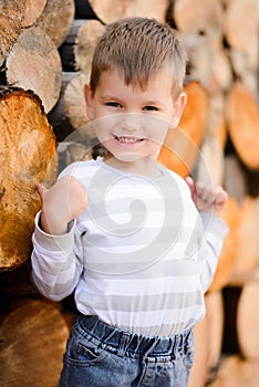 Smiling blond boy showing thumb up standing on a wooden background