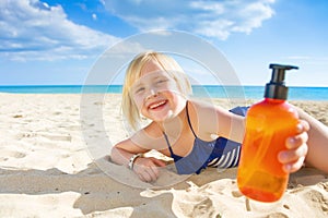 Smiling blond child in swimsuit on seashore showing sun screen