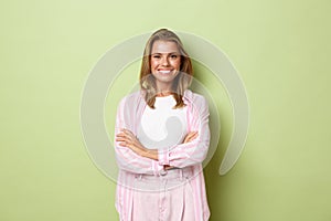 Smiling blond girl in pink outfit looking confident, cross arms over chest, standing against green background