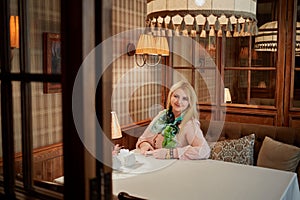 Smiling blond woman sits alone at table in cosy photo