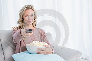Smiling blonde changing tv channel while eating popcorn