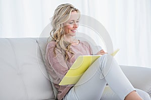 Smiling blonde on couch taking notes on notebook