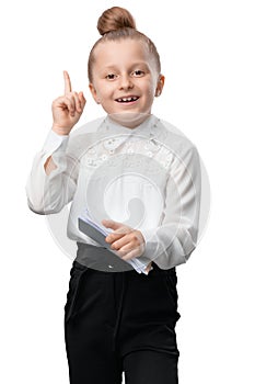 A smiling blonde elementary school student in a school uniform holds notebooks shows her index finger up demonstrating an idea or