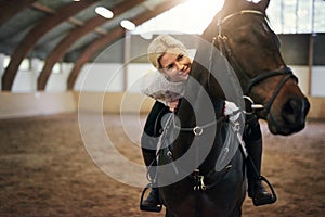 Smiling blonde female leaning on black horseback