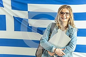 Smiling blonde female student wearing braces stands in front of flag of Greece