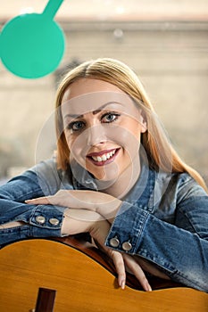 Smiling blonde haired woman leaning over guitar.