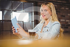 Smiling blonde having coffee and using tablet computer
