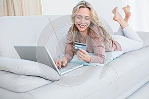 Smiling blonde lying on couch shopping online