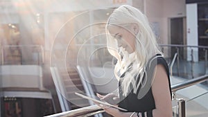 Smiling blonde model woman with shopping bags using tablet computer at shopping mall, fashion student girl