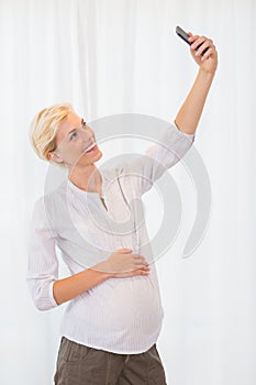 Smiling blonde pregnant woman taking a selfie