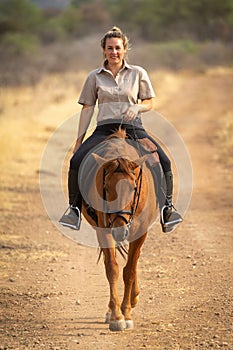 Smiling blonde rides horse along dirt track