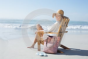 Smiling blonde sitting on wooden deck chair by the sea