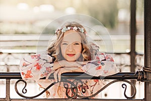 Smiling blonde teen girl posing in summer garden. Wearing flower wreath outdoors