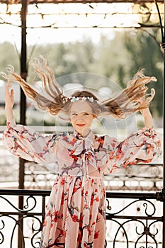 Smiling blonde teen girl posing in summer garden. Wearing flower wreath outdoors