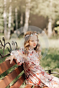 Smiling blonde teen girl posing in summer garden. Wearing flower wreath outdoors