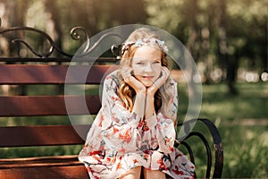 Smiling blonde teen girl posing in summer garden. Wearing flower wreath outdoors