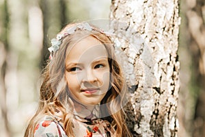 Smiling blonde teen girl posing in summer garden. Wearing flower wreath outdoors