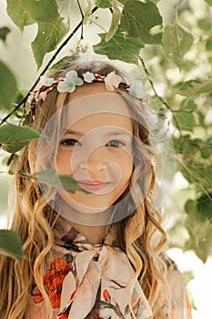 Smiling blonde teen girl posing in summer garden. Wearing flower wreath outdoors