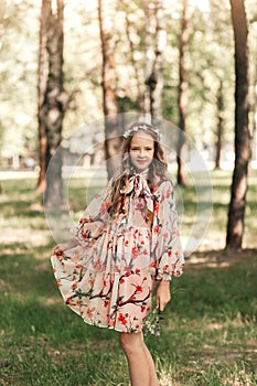 Smiling blonde teen girl posing in summer garden. Wearing flower wreath outdoors