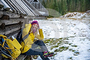 A smiling blonde tourist in a yellow down jacket is wearing crampons for shoes.