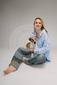 Smiling blonde woman in a blue shirt sits on the floor, the dog sitting on her laps